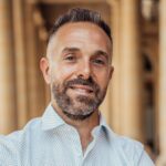 Portrait of a confident adult male in a light blue shirt, posing in a Parisian colonnade.