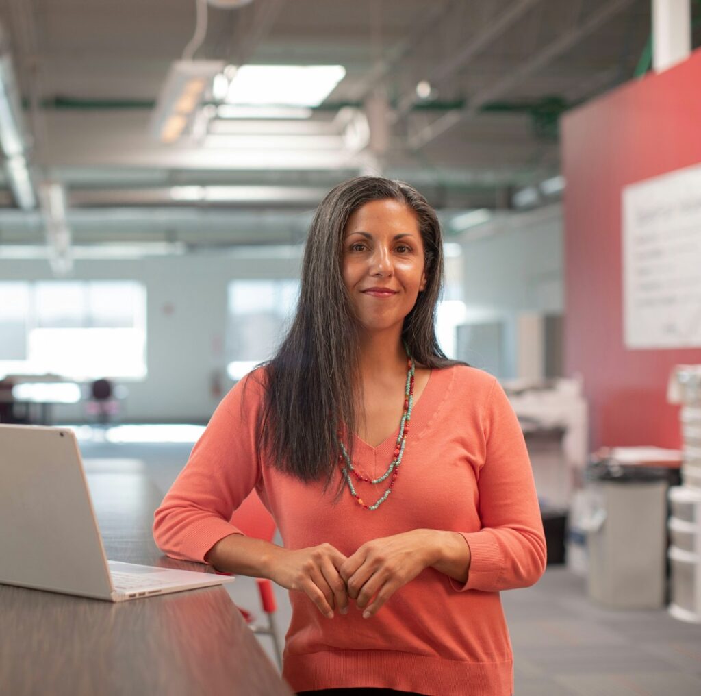 woman in orange long sleeve shirt sitting beside table with macbook pro