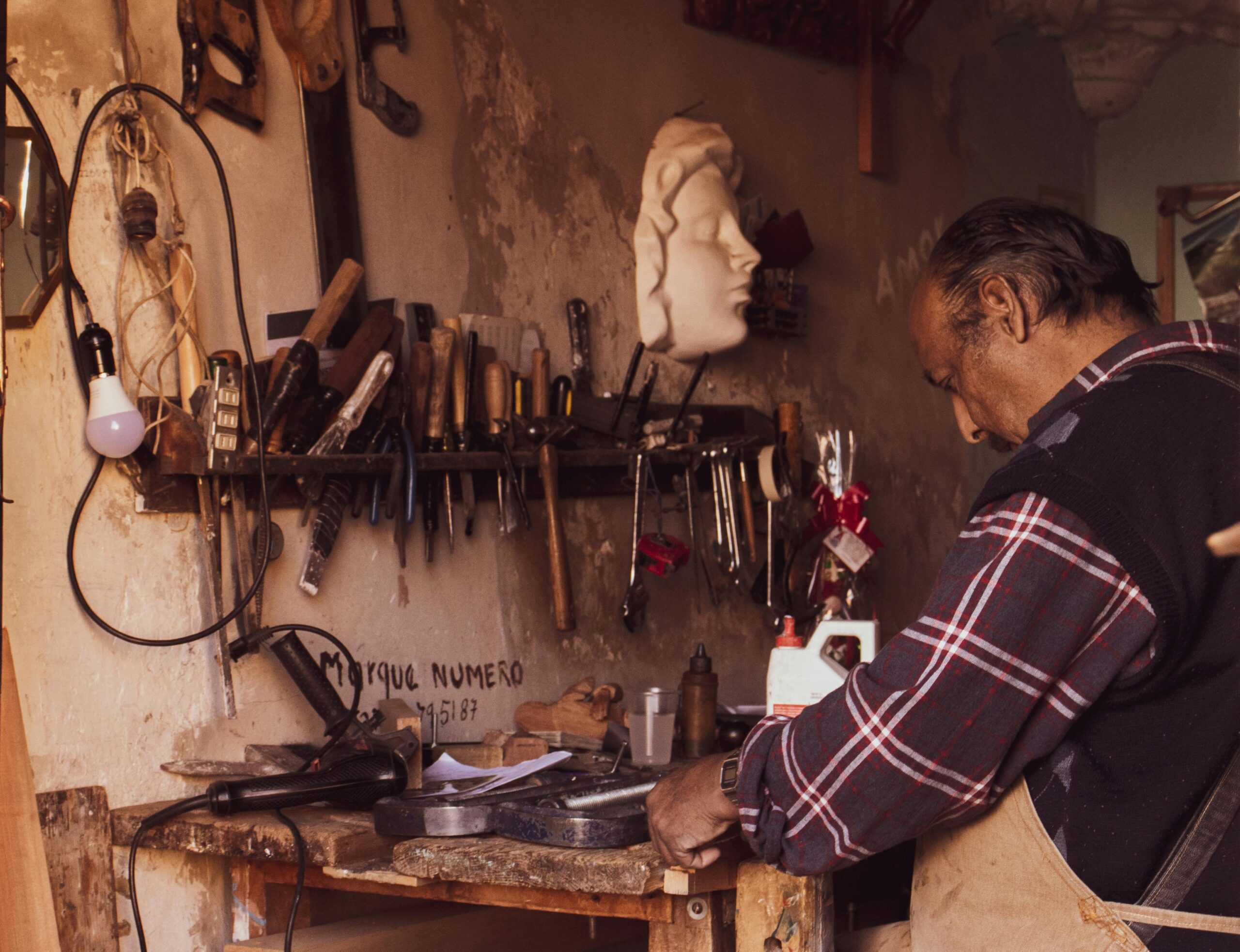 Craftsman focused on work in vintage workshop with tools and sculptures.