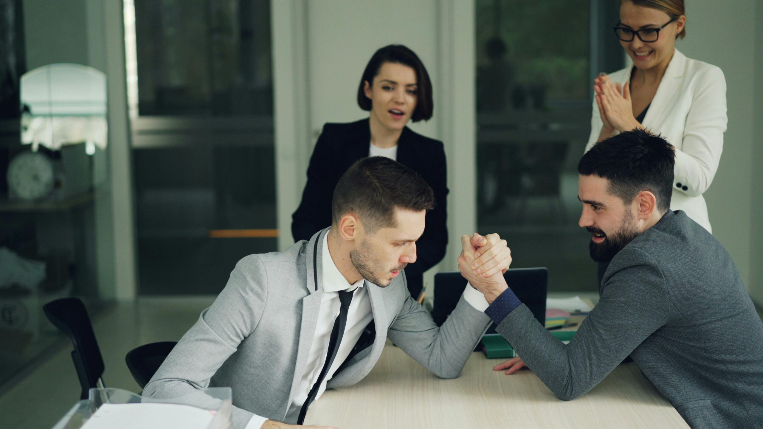 Colleagues cheering for a friendly office arm wrestling match among team members.